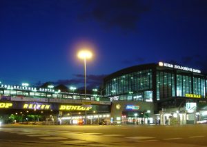 Night view of Berlin Zoologischer Garten train station, brightly lit with neon signs and an arched bridge featuring "Dunlop" advertisements.