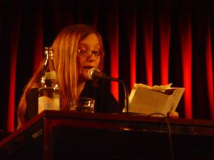 an author reading from a book in front of a red curtain